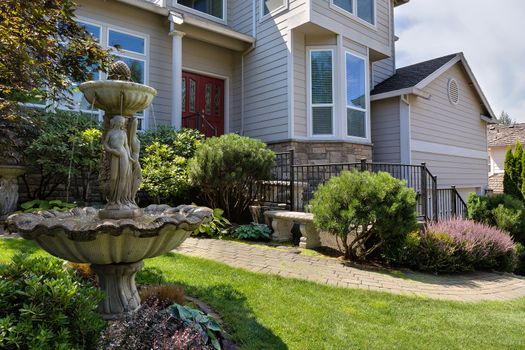 Residential single home in North America suburbs frontyard with manicured garden green lawn paver brick walkway bench and stone water fountain