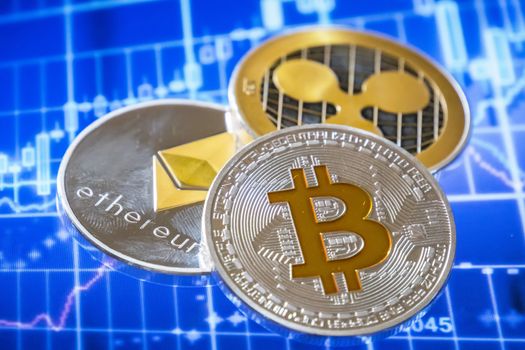 Cryptocurrency coins over trading graphic screen; Bitcoin, Ethereum and Ripple coins