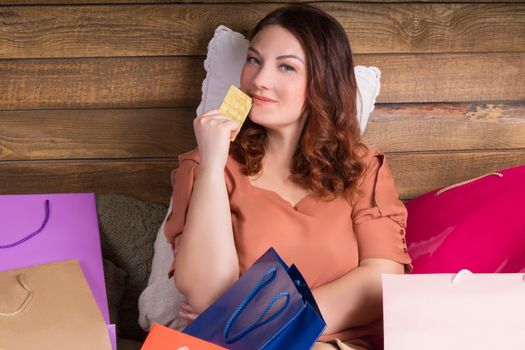 Woman after shopping sits on bed with paper bags showing banking credit card