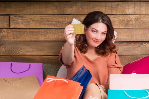 Woman after shopping sits on bed with paper bags showing banking credit card