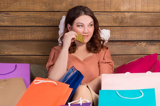 Woman after shopping sits on bed with paper bags showing banking credit card