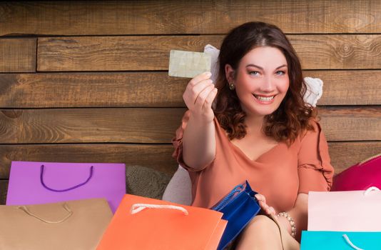 Woman after shopping sits on bed with paper bags showing banking credit card