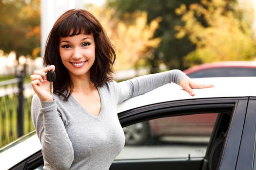 Happy owner of a new car, smiling cute young girl showing a key