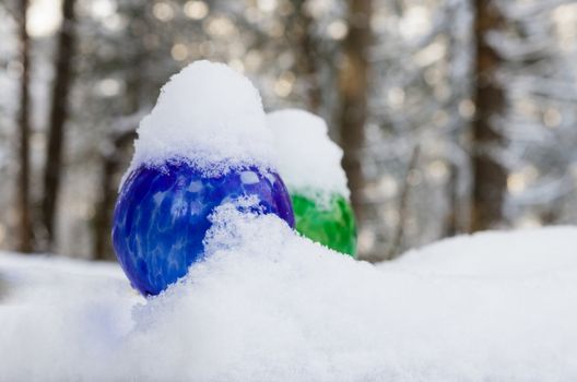 Colorful watering globes covered in fresh snow on a winter day with trees in the background