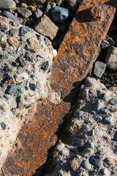 Rusty iron bar impregnated between rocky concrete blocks with a bolt visible