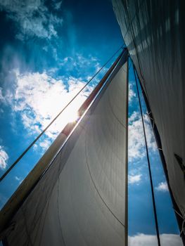 White sail against blue sky, clouds and sun ray