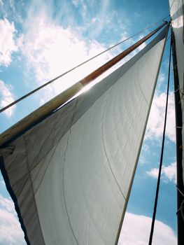 White sail against blue sky, clouds and sun ray