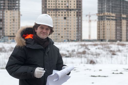 Worker or engineer holding drawing in hands and reading it on background of new apartment buildings and construction cranes on background. Architect engineer concept. Soft focus