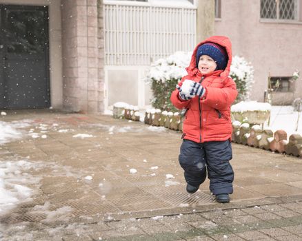 Baby boy while it snows runs with a snowball in his hands