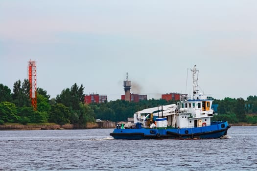 Blue tug ship moving to the cargo terminal. Industrial services