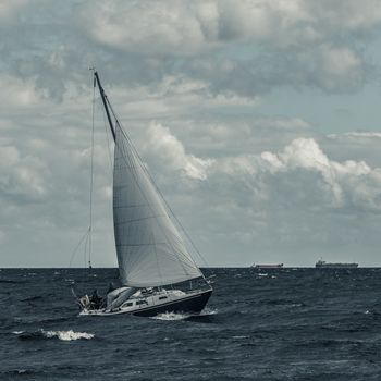Blue sailboat in a travel at stormy sea. Regata journey. Toned