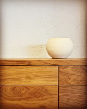 White ceramic vase decorating a wooden chest of drawers. Modern design.
