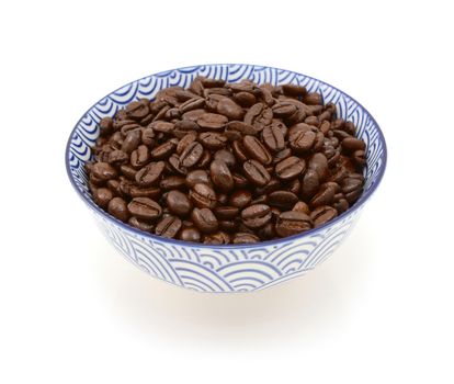 Roasted coffee beans in a blue and white ceramic bowl, on a white background