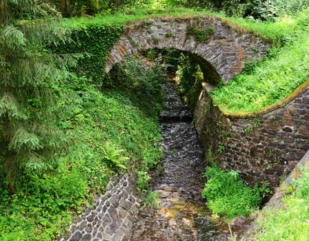 Wild stream flowing under an old stone bridge in nature.