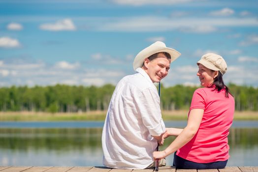 happy couple with a fishing rod sitting on a wooden pier near the lake