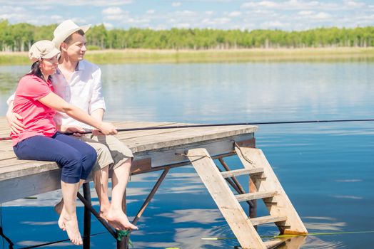 happy couple on the pier with bare feet catching fish on a beautiful lake