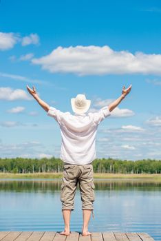 the man on the pier with his arms stretched out to the sides enjoying the beautiful nature near the lake, the view from the back