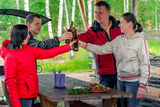 company of friends with beer and tasty shish kebab in the nature on a picnic