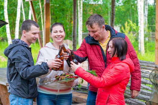 Four friends having a picnic with beer and barbecue on nature