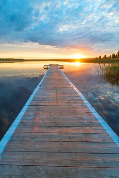 vertical photo of a beautiful landscape - a long wooden pier and a setting sun over a picturesque lake