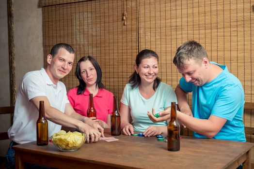 happy four friends while playing poker at the table and drinking beer