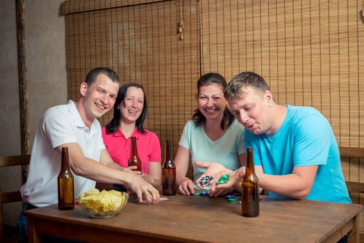 young and happy four friends while playing poker at the table and drinking beer