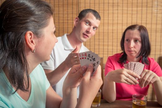 man and two women playing poker, a woman showing their cards