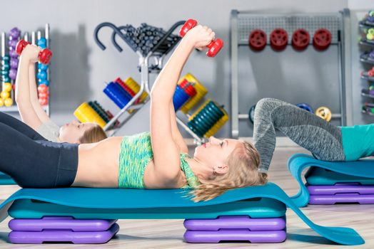 woman lifting dumbbells lying down, class at the gym in a group
