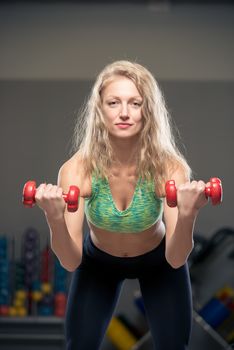 beautiful blonde performing exercises with dumbbells in the gym