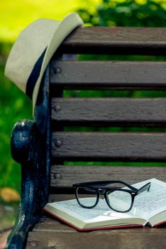 an interesting book, glasses and a beige straw hat were left on a bench in the park