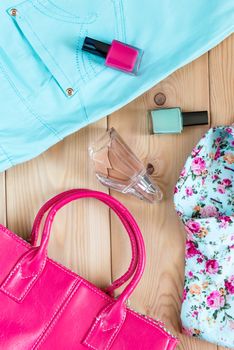 nail polish, perfume, pink bag, shirt with floral print and turquoise trousers - set top view