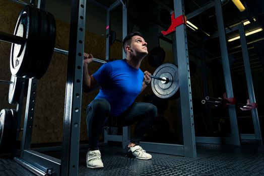 bodybuilder in a blue T-shirt with a barbell in the gym, dark photo