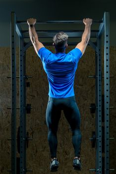 view from the back of an athlete pulls up on the bar in the gym