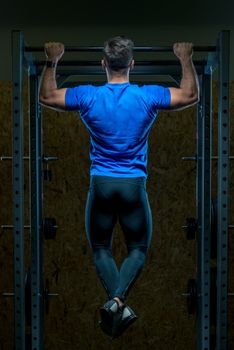 strong athlete pulls up on the bar in the gym view from the back