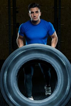 portrait of a strong athlete with a large heavy wheel in the gym