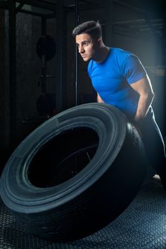 vertical portrait of a focused athlete posing with a heavy wheel in the gym