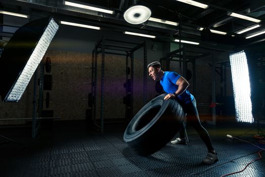 dark photo of a strong bodybuilder with a heavy wheel in the gym