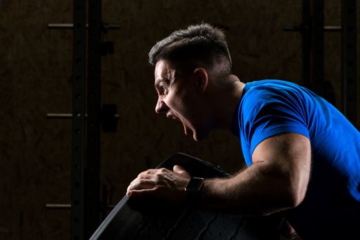 screaming sportsman bodybuilder lifts a heavy heavy wheel, close-up portrait