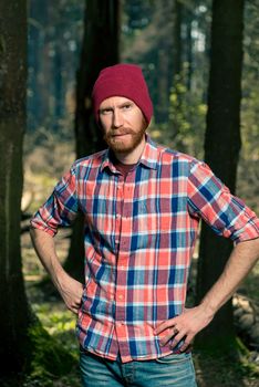 portrait of a serious man with a beard in a plaid shirt and hat in the woods