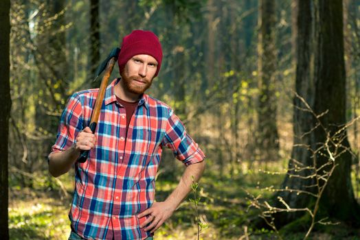 portrait of a forester with a beard and an ax in a shirt in the woods