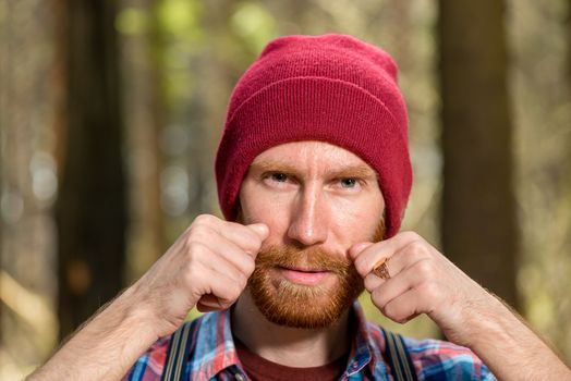 close-up portrait of a man in a hat who adjusts his mustache