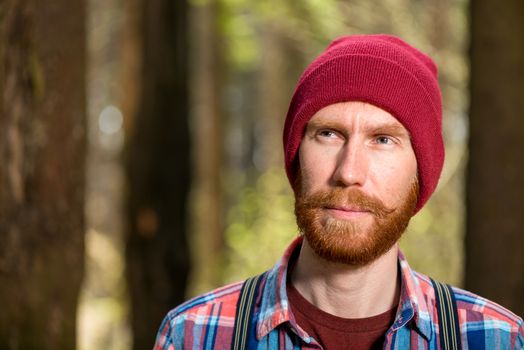 pensive portrait of a bearded man in a red hat in the forest