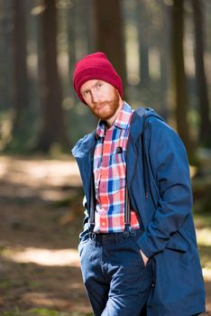 Vertical portrait of a stylish man with a beard wearing a hat and jacket posing in forest