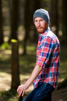 vertical portrait of a serious forester hipster with a beard with an ax in the woods