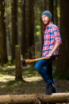 thoughtful forester with an ax near a dumped tree in the forest