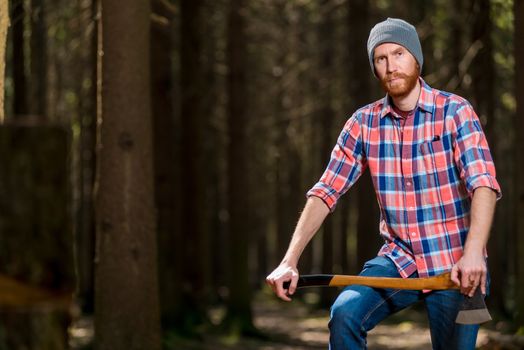 a forester with a beard in a checkered shirt posing in a forest with an ax