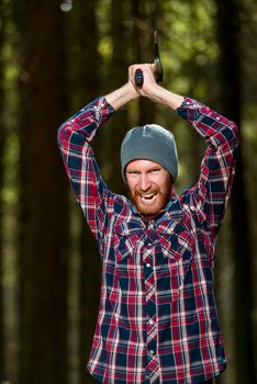 An aggressive bearded woodcutter with an ax chopping wood into the woods