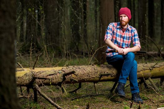 forester with a beard resting on a fallen tree in the forest