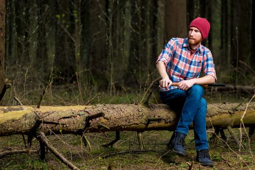 a brooding forester with a beard resting on a fallen tree in the forest