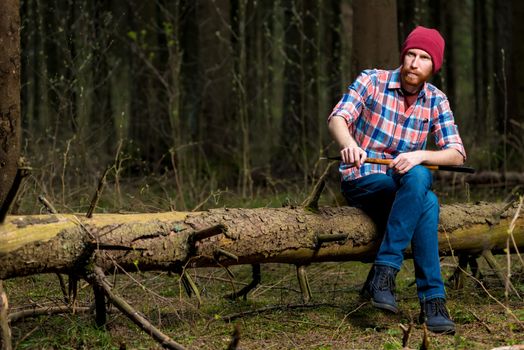 portrait of a forester in a plaid shirt with an ax sitting on a log